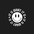 A white circular sticker or decal featuring a simple smiley face in the center with the phrase 'IT IS WHAT IT IS' written around it in a bold, curved font, set against a solid black background.