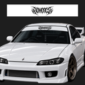 A white modified sports car shown from the front three-quarter angle on a dark studio background, with a black stylized 'Savage' decal displayed on the windshield and a matching decal sheet shown above. The car has a large front splitter, a prominent grille, aftermarket wheels, and 'BRIDE' printed on the seats.