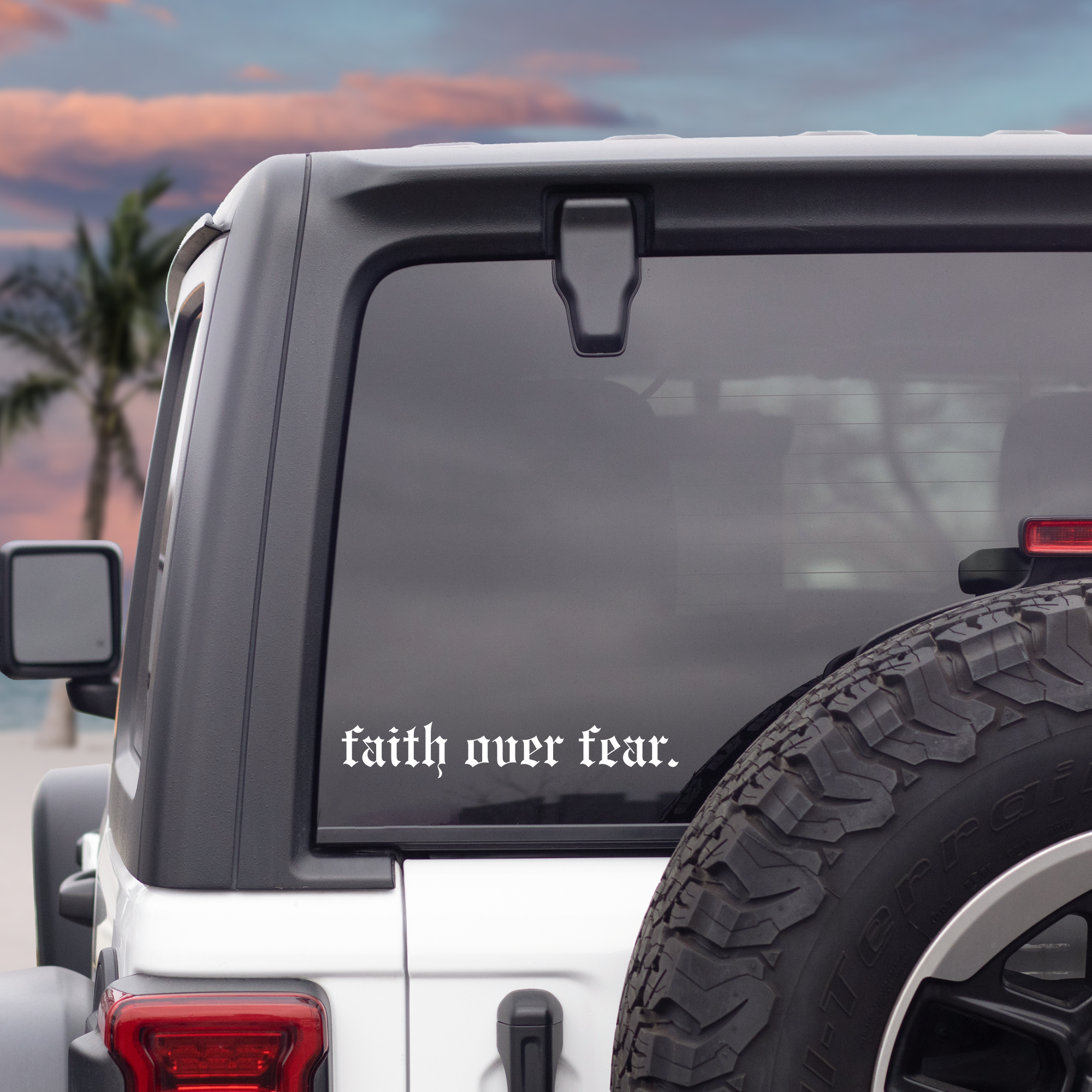 White SUV with 'faith over fear' decal on the back window, palm trees, and sunset in the background.