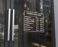Store hours decal on glass storefront door displaying business hours in white vinyl lettering